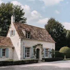 a white brick house with blue shutters on the front and side windows, surrounded by hedges