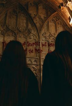 two people standing in front of a wall with writing on it