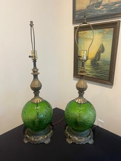 two green glass lamps sitting on top of a black table next to a framed painting