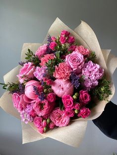 a bouquet of pink and purple flowers is held by someone's hand on a gray background