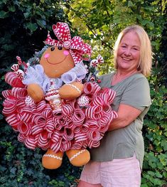 a woman is holding a wreath made out of candy canes and a teddy bear