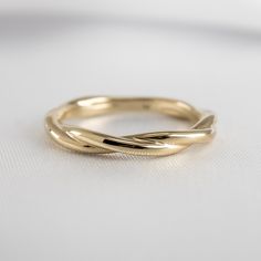 a yellow gold wedding ring on a white surface with the top part of it curled up