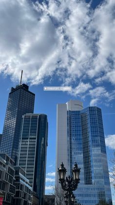 some very tall buildings in the city under a blue sky with white clouds above them