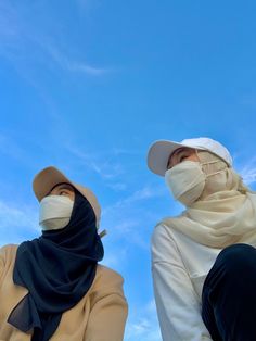 two women wearing face masks and sitting against a blue sky