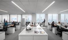 an office filled with lots of desks and people sitting at computers in front of large windows