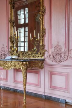 an ornately decorated table with a mirror on it in front of pink painted walls