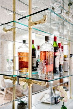 several bottles and glasses are lined up on the glass shelving in this bar area