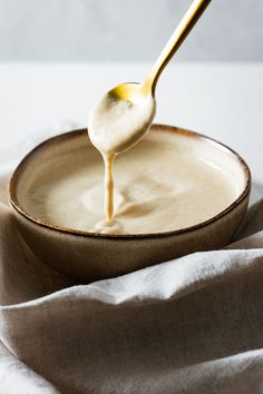 a spoon full of cream being drizzled on top of a bowl with a cloth