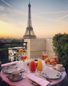 the table is set with breakfast and drinks in front of the eiffel tower