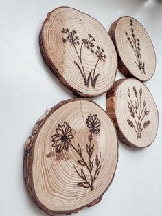 four wood slices with flowers on them sitting on top of a white tablecloth covered surface