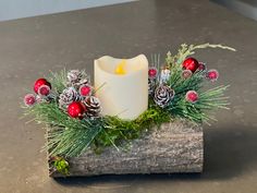 a white candle sitting on top of a wooden block filled with pine cones and berries