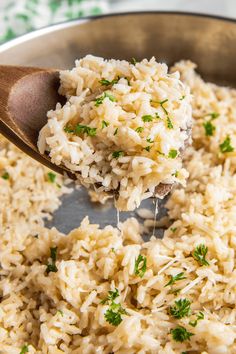 a wooden spoon scooping rice out of a pot with some parsley on top