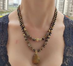 This gorgeous natural agate pendant necklace is the perfect addition to any jewelry collection. The unique design features a stunning brown tiger eye beaded layered necklace that is sure to turn heads. Each bead is carefully handpicked and strung together to create a one-of-a-kind piece that is truly elegant. The boho design of this necklace makes it a versatile accessory that can be dressed up or down, making it perfect for any occasion. The agate stone is known for its grounding properties, making it a great choice for those who need a little extra balance in their lives. The brown tiger eye beads add a touch of warmth and positivity, making this necklace a great choice for those who need a little extra motivation and inspiration. This necklace is the perfect gift for Valentine's Day or Eyes Necklace, Jewelry Valentines Day, Brown Tiger, Tiger Eyes, Brown Tiger Eye, Agate Pendant Necklace, Tigers Eye Necklace, Tiger Eye Beads, Necklace Beaded