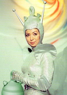 a woman in a silver outfit with two antennae on her head and hands out to the side