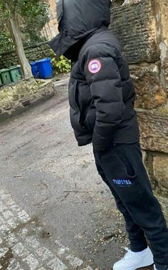 a person wearing a black jacket and white shoes standing in front of a stone wall