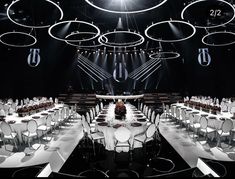 a room filled with tables and chairs covered in white tablecloths, surrounded by round chandeliers