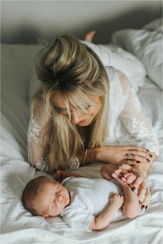 a woman laying on top of a bed next to a baby in her arms and holding it