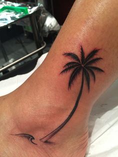 a small palm tree tattoo on the leg with waves coming up from it's top