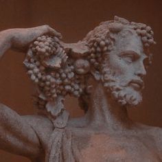 the statue has grapes on his head and is holding it in one hand with both hands