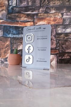 a remote control sitting on top of a table next to a brick wall and potted plant