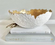 a white and gold bowl sitting on top of two books