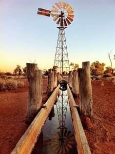 an old windmill sitting on top of a dirt field next to a body of water