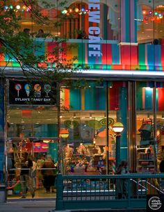 people are walking in front of a brightly lit storefront at night with colorful lights on the windows