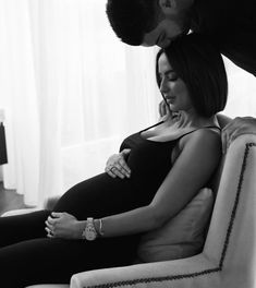 a pregnant woman sitting on top of a couch next to a man kissing her belly