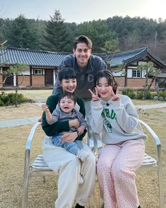 a man and two children sitting on a chair in front of a house with their fingers up