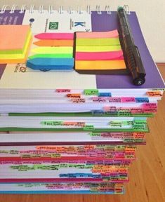 a stack of notebooks with colored sticky notes on them and a pen resting on top