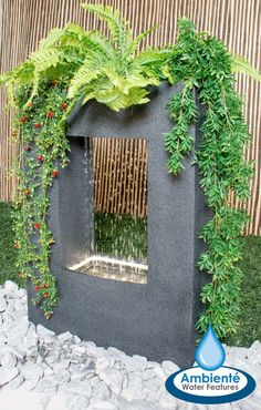 an outdoor fountain with plants and water running down it's sides, surrounded by rocks