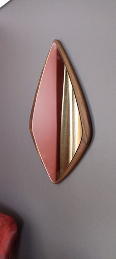 a mirror mounted to the side of a gray wall next to a red leather chair