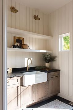 a kitchen sink sitting under a window next to a wooden cabinet and counter top in a room