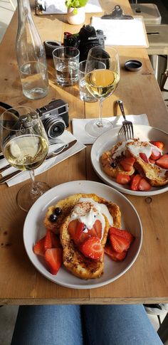 two white plates topped with french toast and strawberries next to glasses of wine on a wooden table