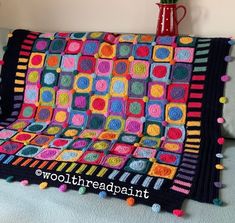 a crocheted blanket with multicolored squares and pom - poms