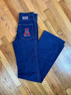 "1970s 80s University of Alabama Crimson Tide Blue Denim Jeans 26\" Waist TALL  University of Alabama patch on rear pocket Straight leg semi boot cut ish Front and back pockets  High waist Fits best on someone with slender hips, less curves  Waist: 26\" / 27\" - 28\" snug Upper hips: 30\" Hips: 34\" Length: 47\" Inseam: 36\" Rise: 10.5\"//11\" Great condition, there's a few light spots, not sure if they're bleach or chemical stains from older days, see photos" Retro Denim Flare Jeans With Pockets, Vintage Denim Flare Jeans, Retro Flare Jeans For Fall, Vintage Denim Flare Jeans With Five Pockets, Vintage Jeans For Fall, Vintage Cotton Flare Jeans For Fall, Vintage Style Cotton Flare Jeans For Fall, Retro Medium Wash Cotton Jeans, Vintage Denim Flare Jeans With Pockets