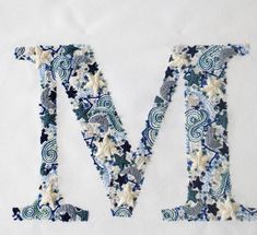 the letter m is made up of blue and white fabric with floral designs on it