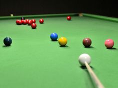 a pool table with several different colored balls on it and one billiard's cue in the foreground