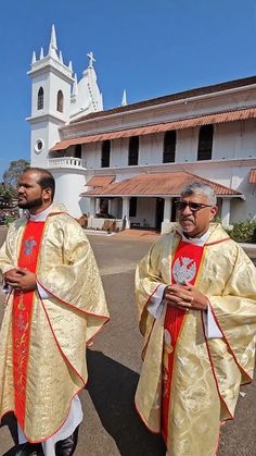 two men standing next to each other in front of a church