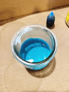 a glass bowl filled with blue liquid next to an empty bottle