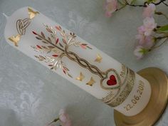 a white candle with gold and red designs on it sitting next to pink flowered branches