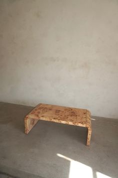 a small wooden table sitting in the middle of a room with concrete flooring and white walls