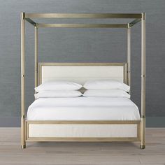 a four poster bed with white linens and gold metal frame, against a gray wall