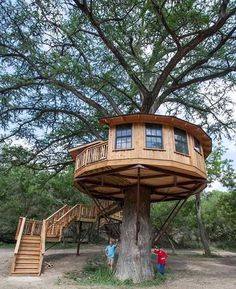 two people standing in front of a tree house with stairs leading up to the top