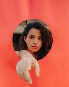 a woman pointing her finger at the camera through a hole in a red paper wall