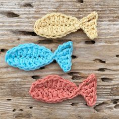 three crocheted bows are sitting on a wooden surface, one is blue and the other is pink