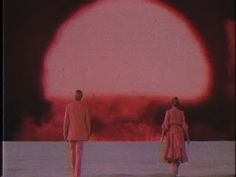 two people standing in front of an orange and red object with the sun behind them