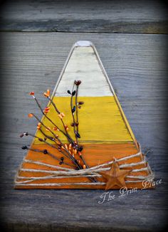 an orange, yellow and white wooden triangle with branches in the center on a wood surface