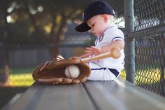 a young boy sitting on top of a wooden bench holding a baseball bat and glove