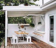 an outdoor dining area with white furniture and wood flooring on a deck overlooking the trees